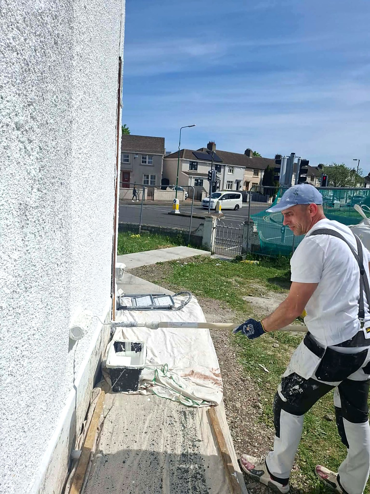 Painter rolling a brilliant white masonry coat onto a pebbledash gable wall